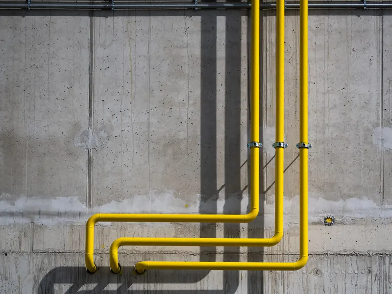 A yellow gas pipe running along a concrete wall