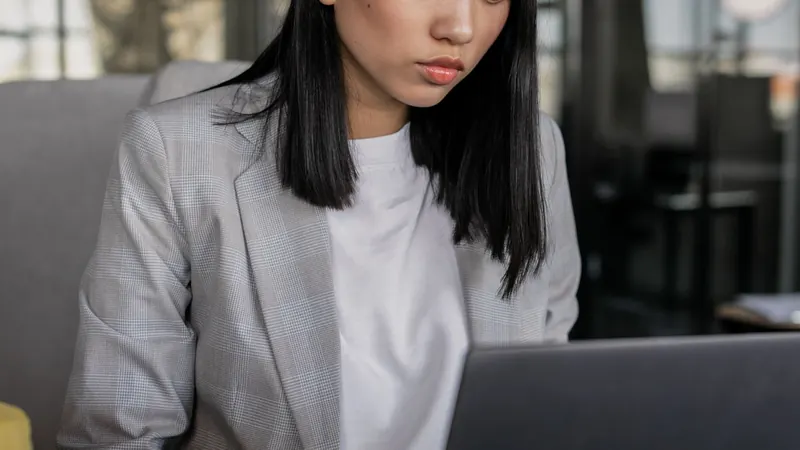 A woman in a grey blazer working on a laptop